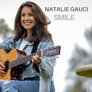 Woman playing guitar outdoors, smiling.