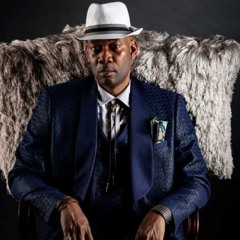 Man in suit and hat sitting on fur chair.